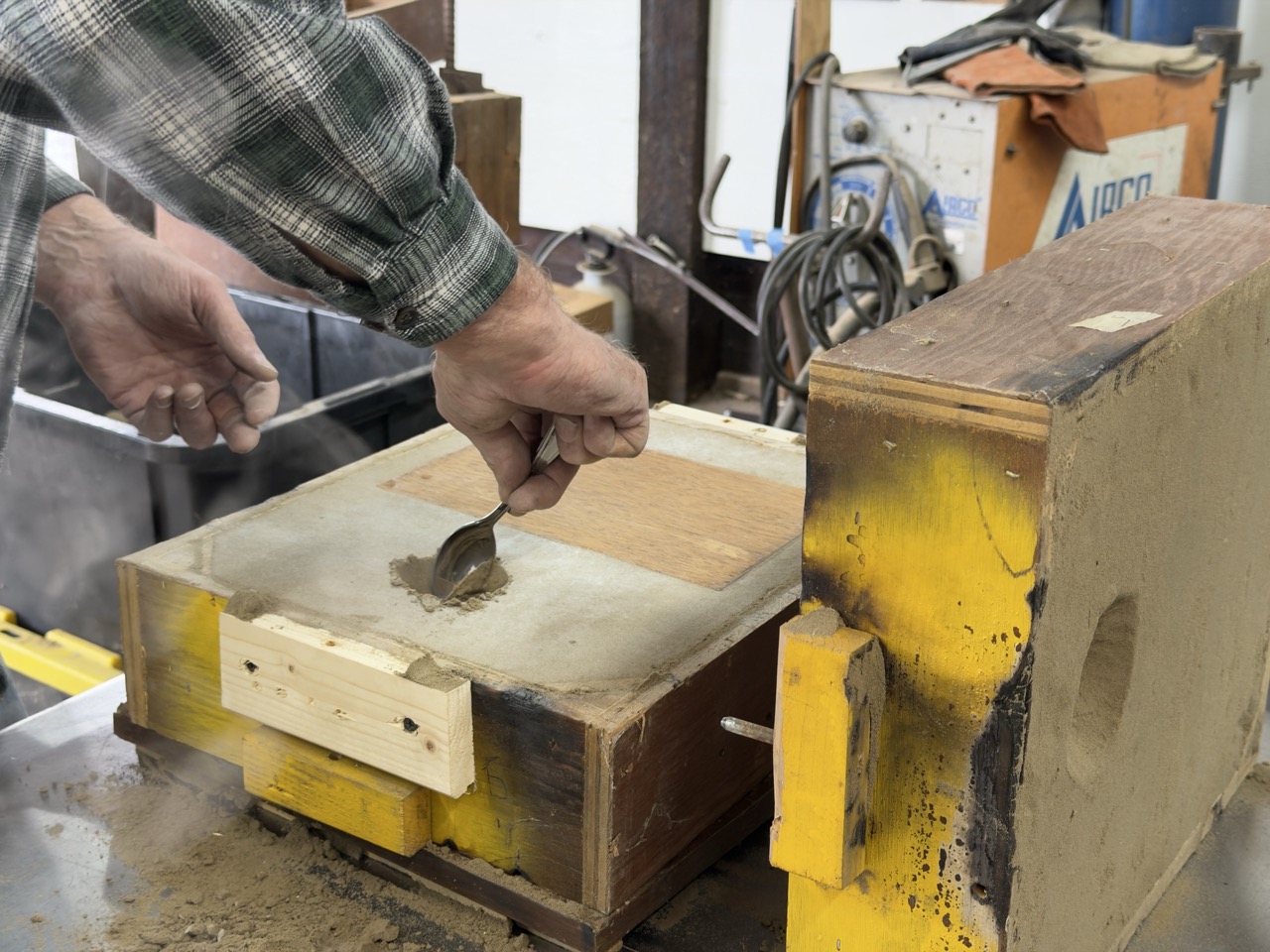A hole in a sand mold being carved with a spoon