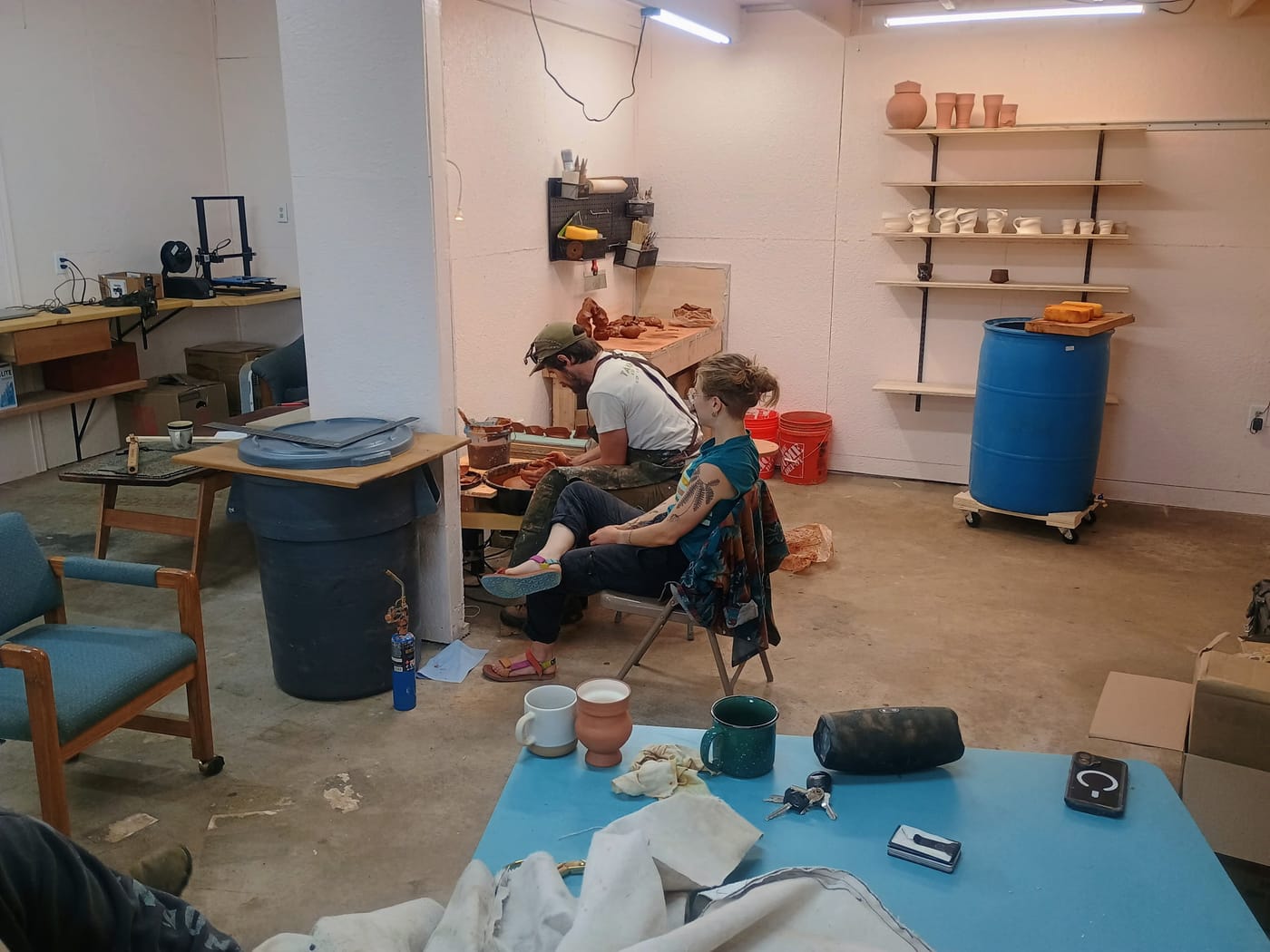 Two people sitting by a pottery wheel, one working on it