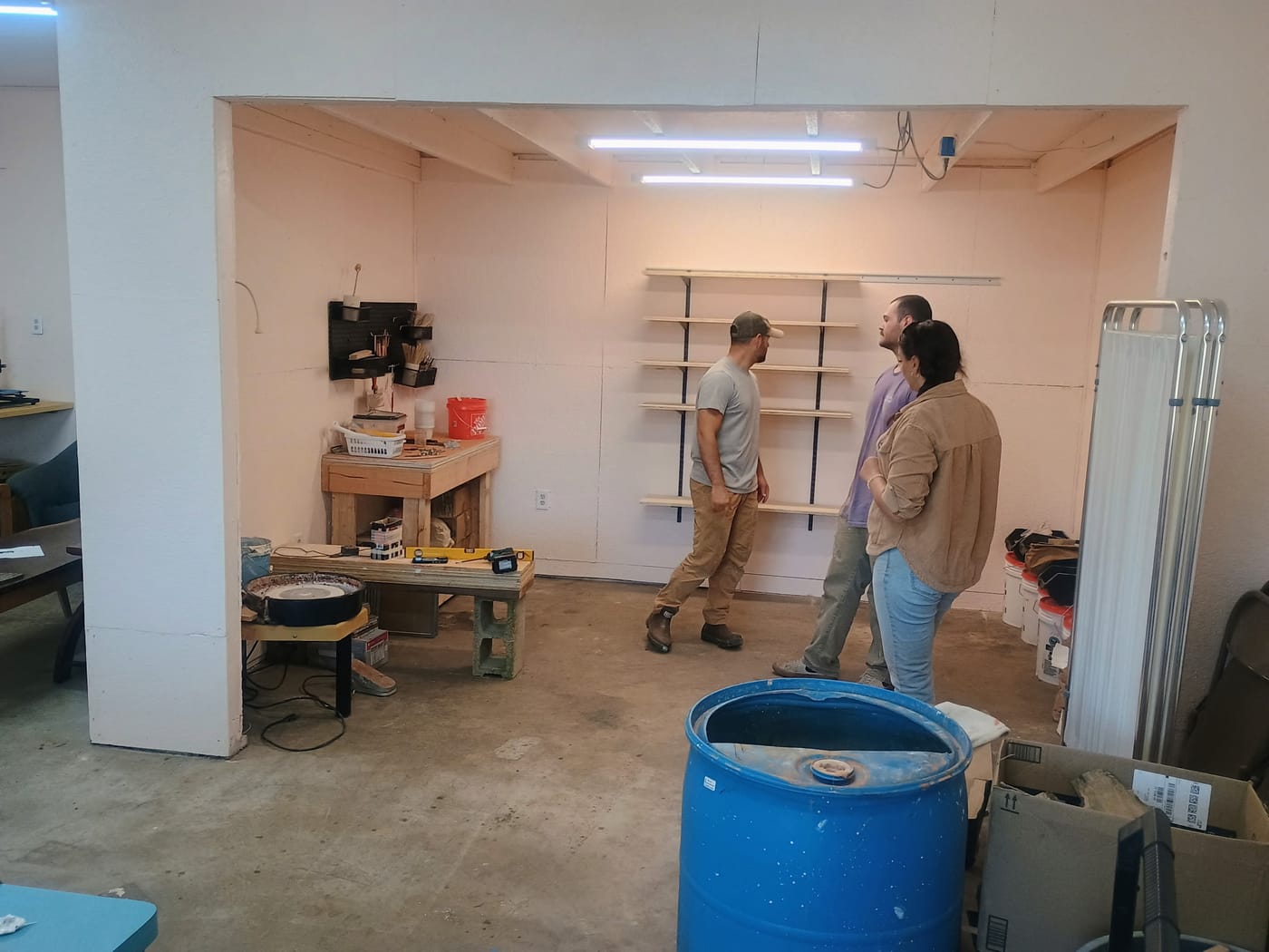Two men and a woman inside the pottery studio, talking